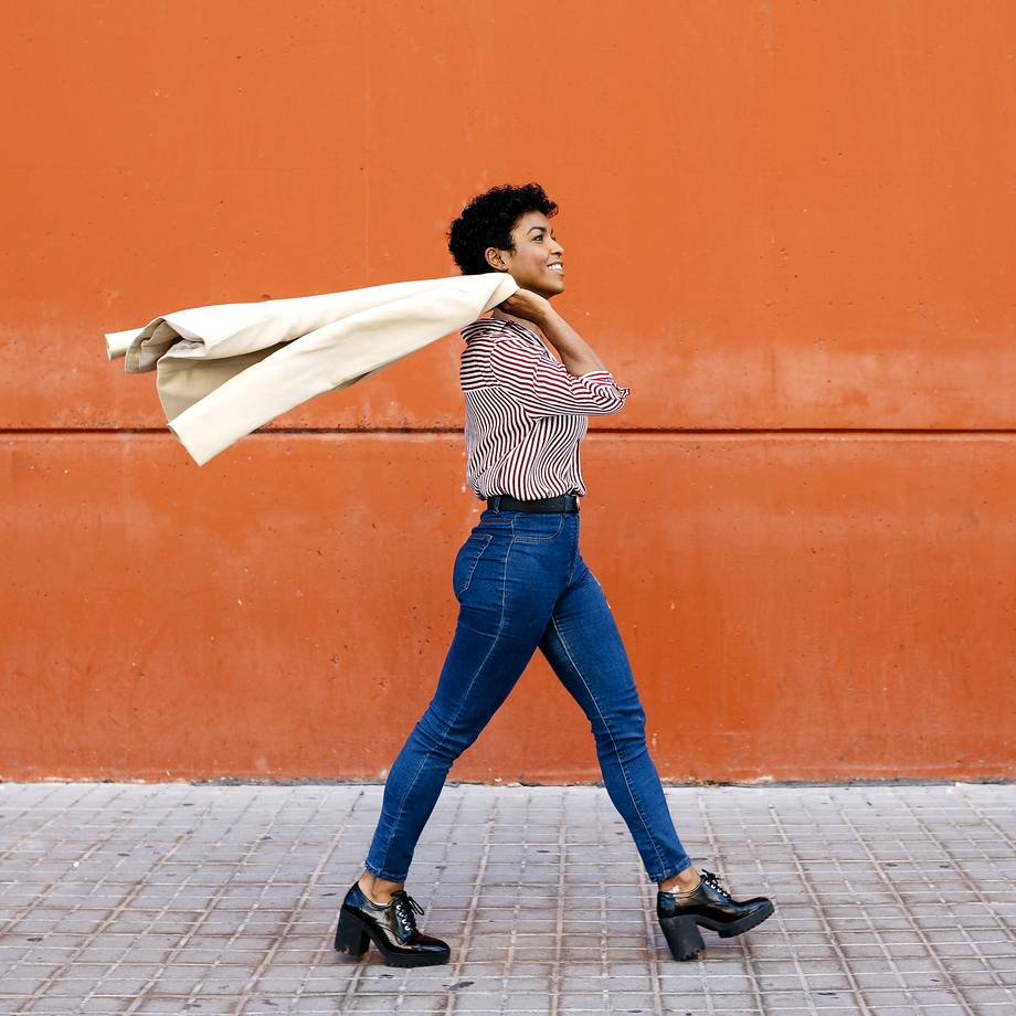 Eine Person läuft vor einer orangen Wand, ein weiße Jacke schwingend.